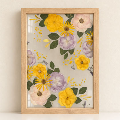 Light oak Just Bloom pressed flower frame with preserved yellow, lilac and blush flowers displayed on a cream shelf.