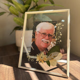 Double-glass memorial frame with a photograph and preserved funeral flowers arranged around the image.