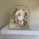 Gold arched double-glass memorial frame with a photograph surrounded by preserved pressed flowers.