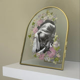 Gold arched double-glass pet memorial frame with a black-and-white photograph surrounded by pink, white and purple pressed flowers.