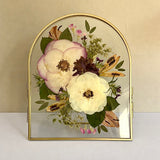 Front view of a Gifting Just Bloom arrangement with pink and white pressed flowers in a gold arch double-glass frame by GLASH Designs