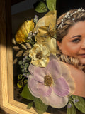 Close-up of a Held in Bloom pressed flower frame with preserved blush and yellow wedding bouquet flowers arranged around a photograph.