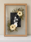 Oak Held in Bloom pressed flower frame displayed on a cream shelf with a black-and-white wedding photo and preserved white bouquet flowers.