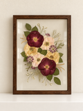 Dark wood Just Bloom pressed flower frame featuring preserved burgundy, blush and cream flowers on a cream ledge