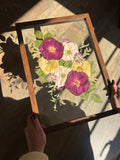Just Bloom pressed flower frame held at an angle in natural light, featuring burgundy, blush and cream flowers.