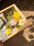 Angled view of a yellow and lilac Just Bloom pressed flower frame held in natural sunlight.