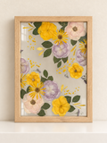 Light oak Just Bloom pressed flower frame with preserved yellow, lilac and blush flowers displayed on a cream shelf.