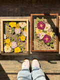 Two custom Just Bloom pressed flower frames displayed side by side on a wooden floor.